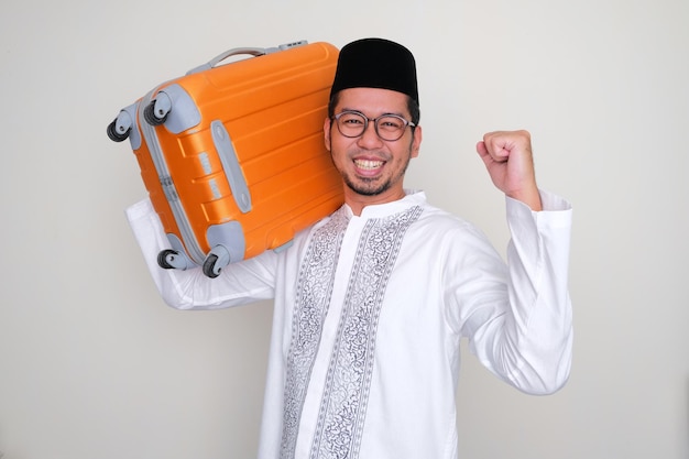 Homem asiático muçulmano rindo animado quando traz uma bagagem no ombro