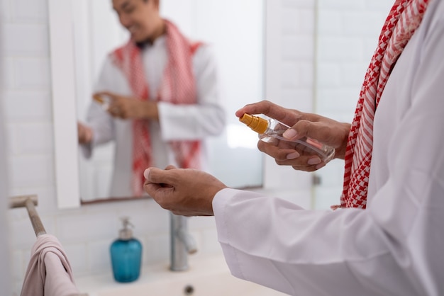 Homem asiático muçulmano se preparando para o eid mubarak. vista-se e aplique perfume no corpo dele