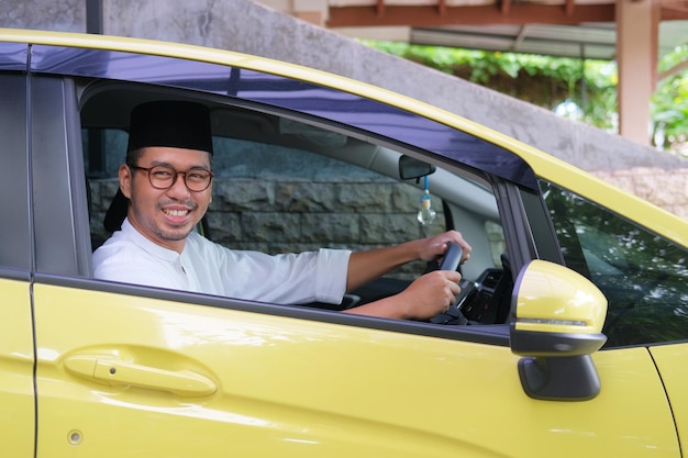 Homem asiático muçulmano sorrindo para a câmera de dentro de seu carro