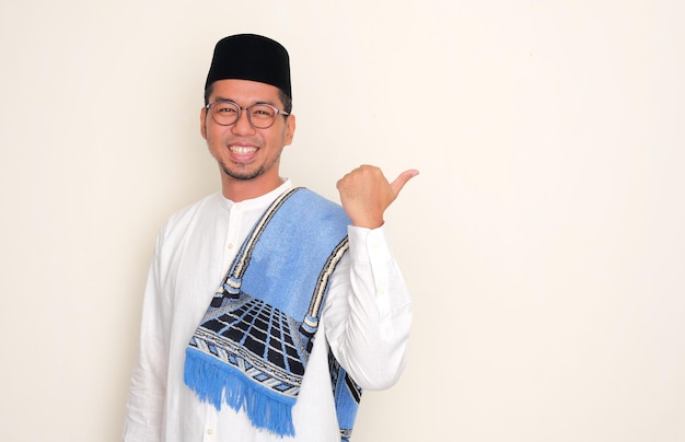 Foto homem asiático muçulmano sorrindo para a câmera e apontando para o lado esquerdo