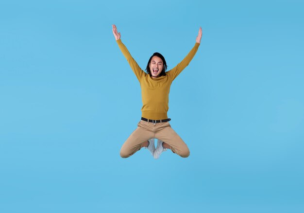 Homem asiático novo energético feliz que salta no meio do ar isolado no espaço azul.