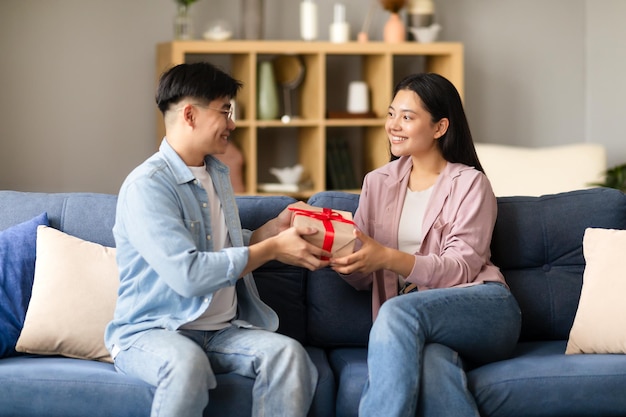 Homem asiático oferecendo presente embrulhado para senhora comemorando feriado dentro de casa