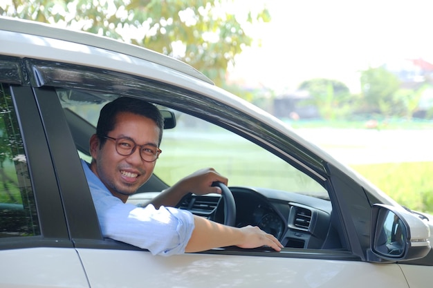 Homem asiático olhando de dentro de seu carro com expressão feliz