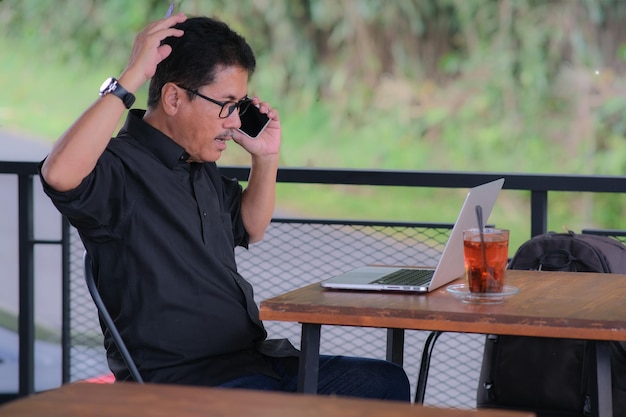Homem asiático olhando surpreso olhando para seu laptop enquanto fala no smartphone