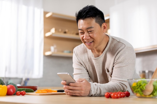 Homem asiático positivo verificando o aplicativo móvel para aprender a cozinhar