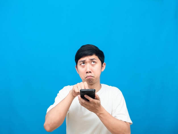 Homem asiático pressiona no celular em sua mão com medo de olhar para o espaço de cópia fundo azul
