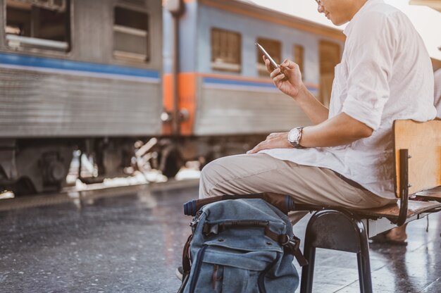 Homem asiático procurando a direção certa no trem station.traveler esperando o trem e planejando as férias de férias com o smartphone. Férias, viagem, viagem e conceito de viagens de verão.