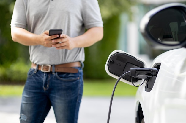 Homem asiático progressivo recarrega seu carro EV na estação de carregamento em casa