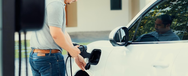 Homem asiático progressivo recarrega seu carro EV na estação de carregamento em casa