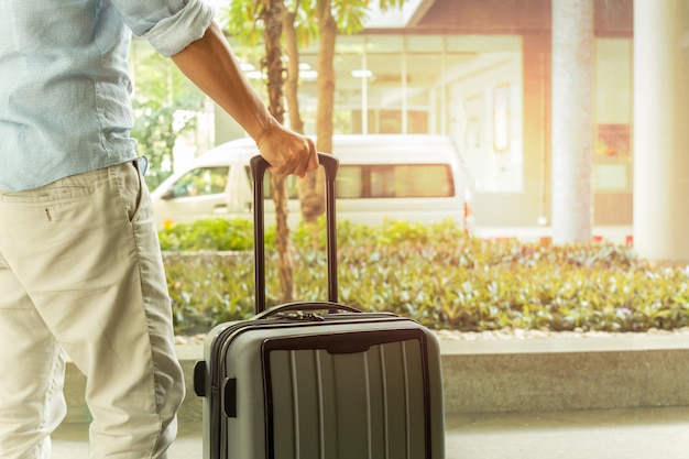 Homem asiático que está com bagagem da mala de viagem no conceito do curso do terminal de aeroporto.
