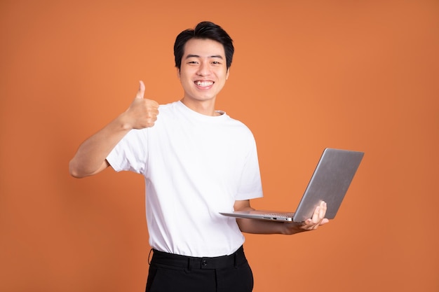 Homem asiático segurando laptop isolado em fundo laranja