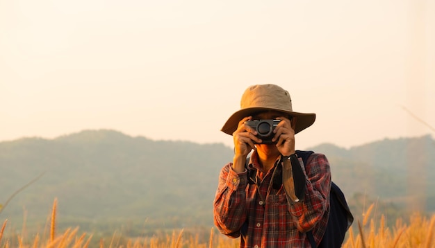 Homem asiático segurando uma câmera com ambos os braços usando um chapéu tirando espaço de fotocópia