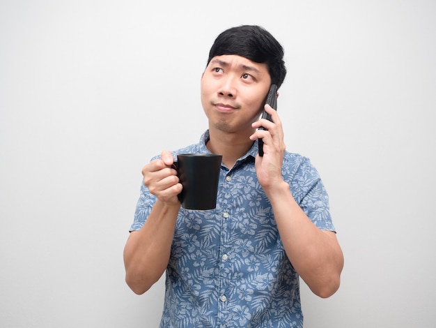 Homem asiático segurando uma xícara de café e falando com gesto de celular feliz