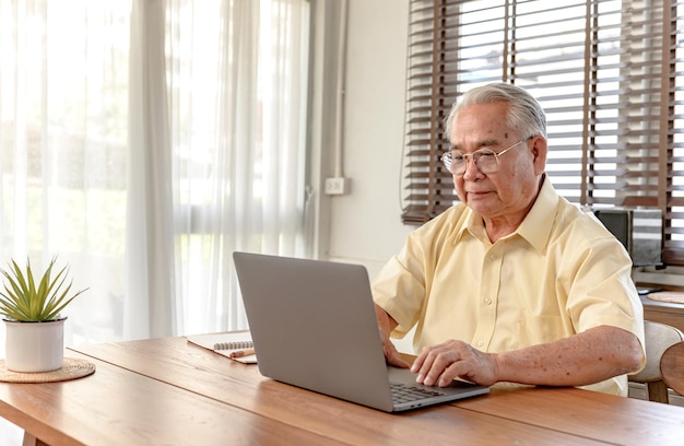 Homem asiático sênior usando laptop e procurando seguro após a aposentadoria. Avô fica sozinho em casa.