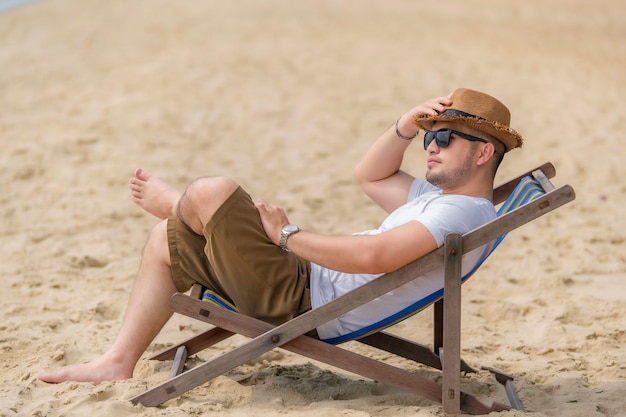 Homem asiático sentado na cadeira de praia dentro do marRelaxe o tempo no verão