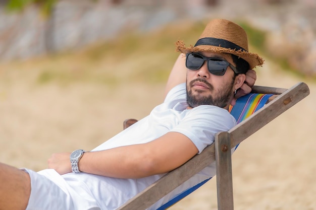 Homem asiático sentado na cadeira de praia dentro do marRelaxe o tempo no verão