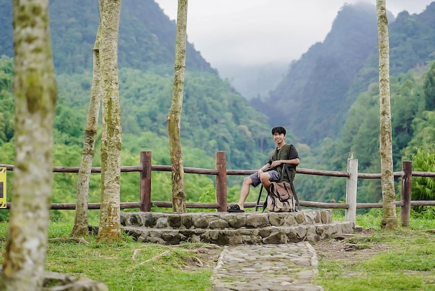Homem asiático sentado sozinho de férias desfrutando de montanhas verdes e frescas