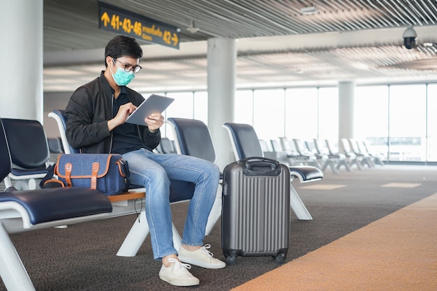 homem asiático sentado sozinho no saguão esperando o horário de embarque da companhia aérea na área de embarque do aeroporto