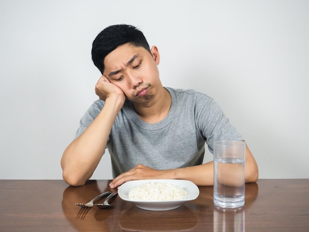 Homem asiático sente comida entediada olhando arroz e água na mesa