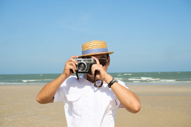 Homem asiático, sentindo-se feliz na praia e céu azul, horário de verão com câmera vintage