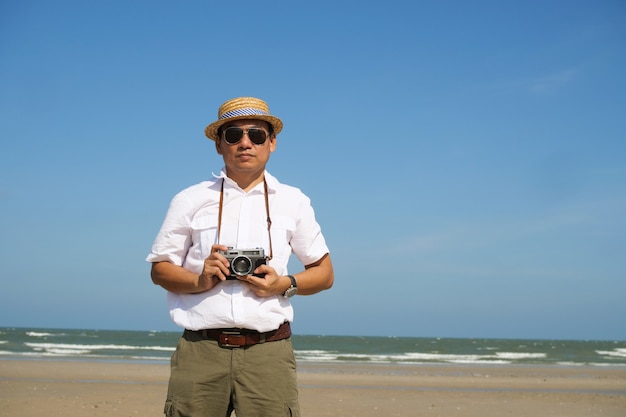 Homem asiático, sentindo-se feliz na praia e céu azul, horário de verão com câmera vintage