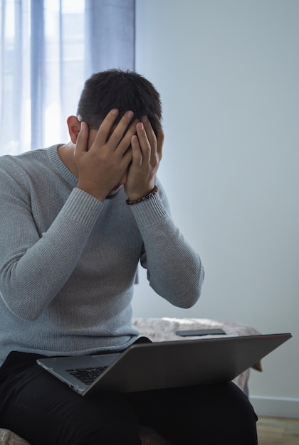 Homem asiático sobrecarregado e exausto escondendo o rosto nas mãos freelancer deprimido em casa com laptop