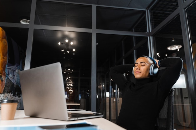 Homem asiático sonolento e cansado trabalhando horas extras no laptop no escritório e descansando