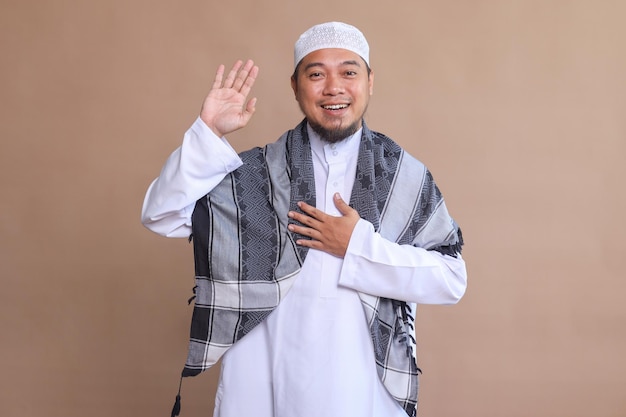 Homem asiático sorridente acenando com a mão para dizer olá e bem-vindo durante o momento do Eid Mubarak