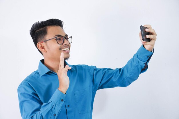homem asiático sorridente ou feliz com óculos segurando smartphone para foto selfie vestindo camisa azul