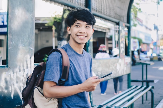 Homem asiático sorridente segurando o celular no ponto de ônibus