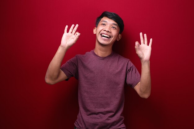 Homem asiático sorrindo com sinal de ok Homem asiático feliz sobre fundo vermelho fazendo sinal de ok