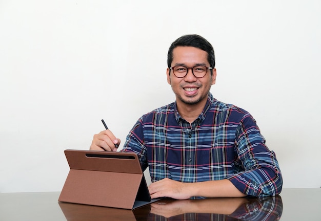 Homem asiático sorrindo para a câmera enquanto trabalhava usando seu tablet móvel