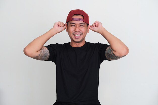 Homem asiático tatuado sorrindo animado ao colocar a tampa para trás na cabeça