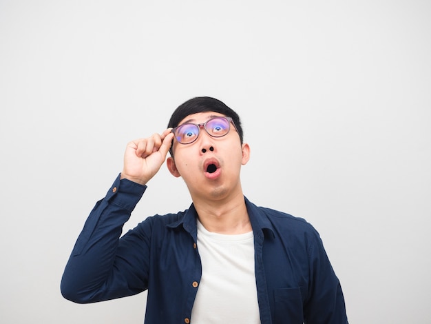 Homem asiático tocando seus óculos, surpreso, olhando para o fundo branco do espaço da cópia