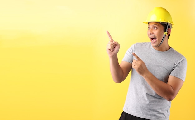 Foto homem asiático trabalhador da indústria ou engenheiro trabalhando um construtor arquiteto apontando o dedo sobre fundo amarelo.