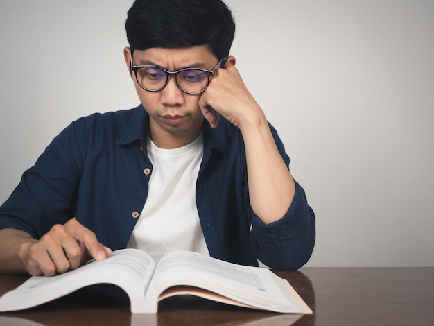 Homem asiático usa óculos, livro de texto de aprendizado sério em cima da mesa