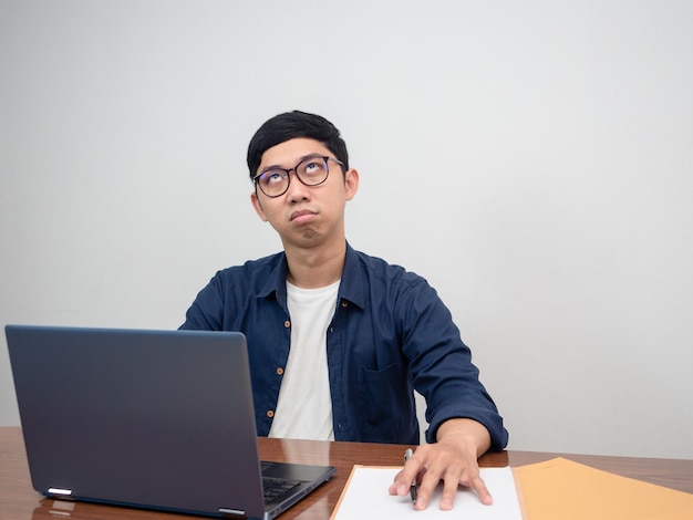 Homem asiático usa óculos sentado na mesa de trabalho se sente entediado com o trabalho