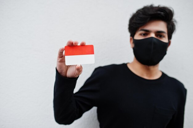 Homem asiático usa todo preto com máscara facial segura a bandeira da indonésia na mão isolada em fundo branco conceito de país coronavirus