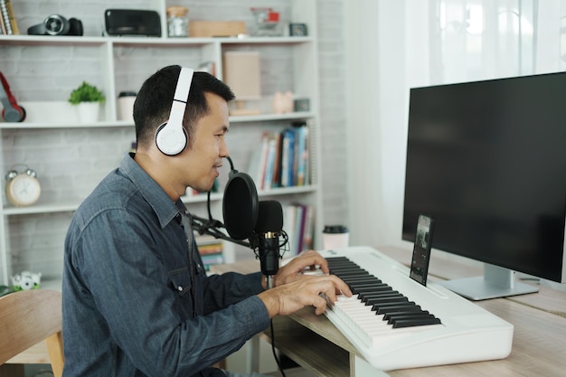 Homem asiático usando fones de ouvido brancos canta uma música aprendendo on-line ou grava som com um microfone e usa programa de gravação de música de computador engenheiro de som homem gravar música