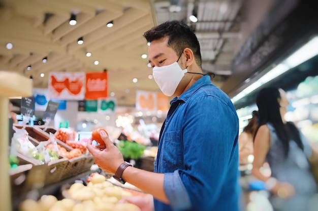 Homem asiático usando máscara cirúrgica andando no supermercado para comprar frutas frescas