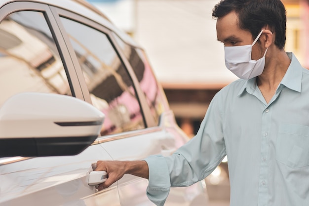 Homem asiático usando máscara facial ao abrir o carro