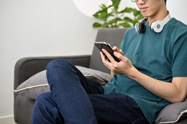 Homem asiático usando um smartphone para conversar com seus amigos enquanto relaxa em sua sala de estar cortada