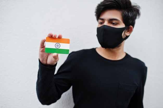 Homem asiático usar tudo preto com máscara facial segurar a bandeira da Índia na mão isolada no branco. Conceito de país do Coronavirus.