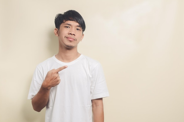 Homem asiático vestindo camiseta branca apontando para o espaço vazio em fundo isolado