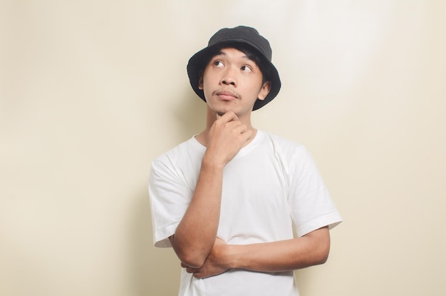 Homem asiático vestindo camiseta branca brilhante com chapéu preto pensando em ideias sobre fundo isolado