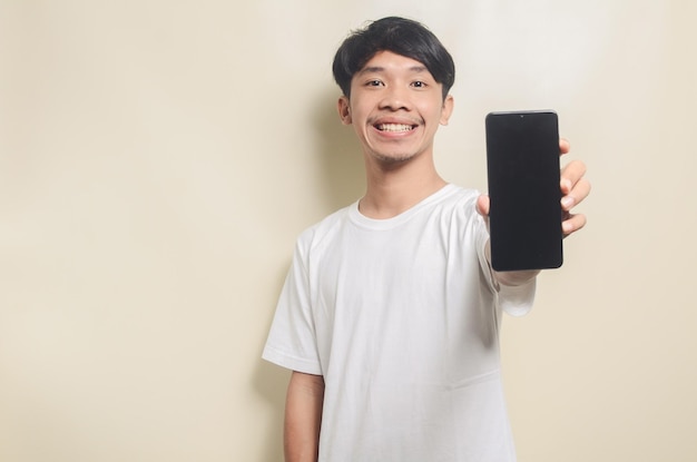 Homem asiático vestindo camiseta branca com gesto mostrando seu telefone em fundo isolado