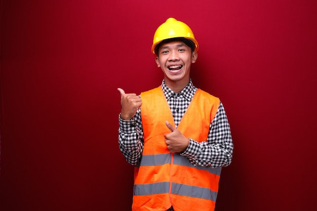 homem asiático vestindo uniforme de contratado e capacete de segurança apontando e aparecendo com o polegar para cima