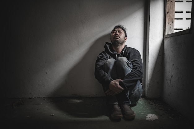 Foto homem asiático viciado em drogas num lugar deserto um viciado sente-se sozinho neste mundo um jovem triste sentado no canto da sala as pessoas estão estressadas e têm depressão