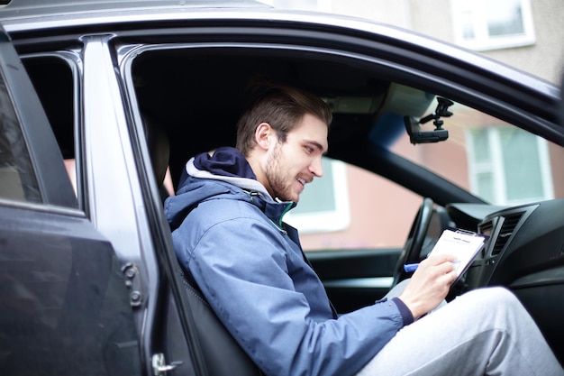 Homem assina um documento enquanto está sentado no carro