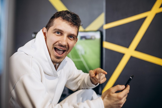 Homem assistindo futebol e usando o celular